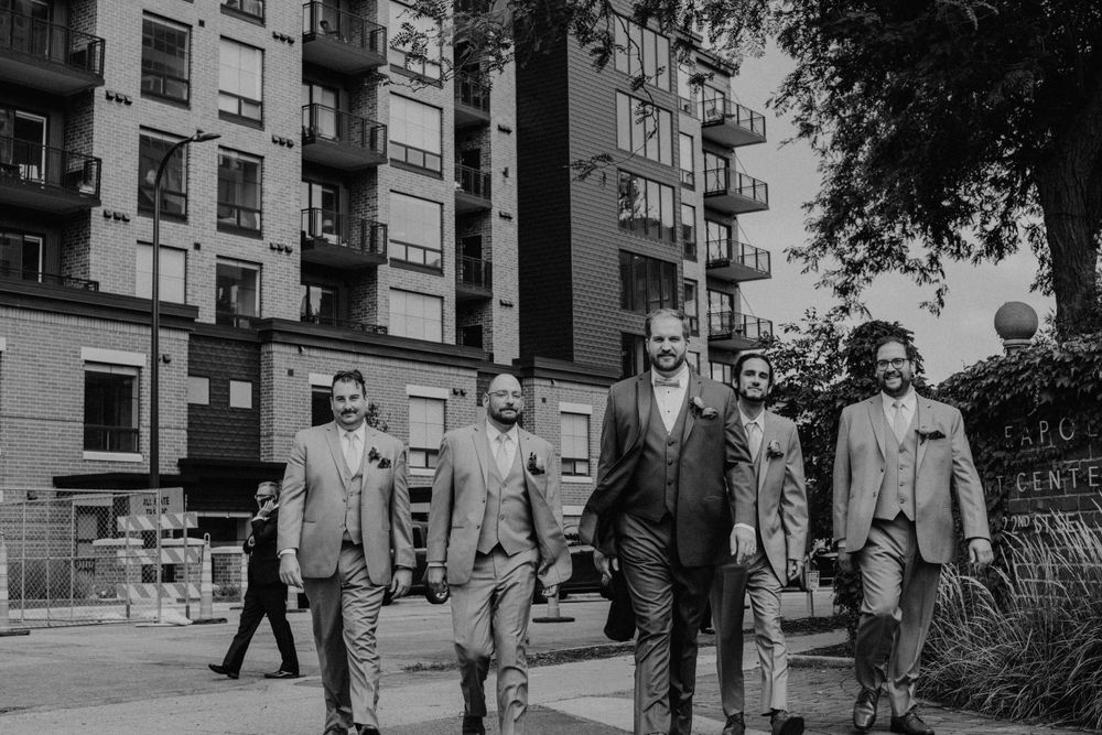 Black and white photo of groom and groomsmen walking together on a city sidewalk.