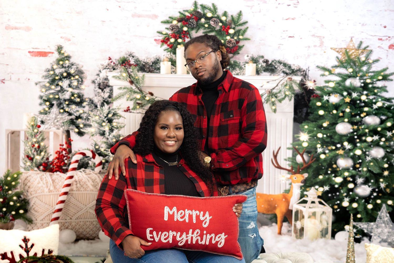 Couple in matching red plaid outfits holding Merry Everything pillow.