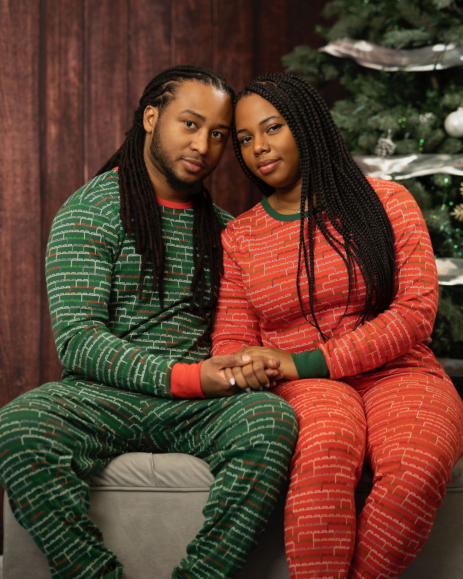 Couple in matching Christmas pajamas holding hands by a decorated tree.