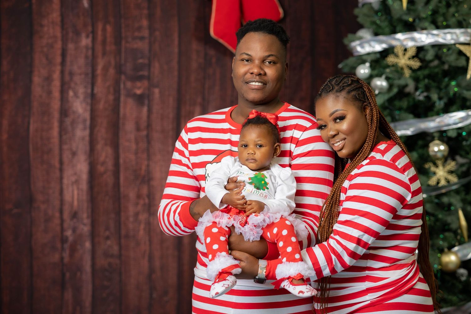 Family of three in red striped pajamas posing by Christmas tree.