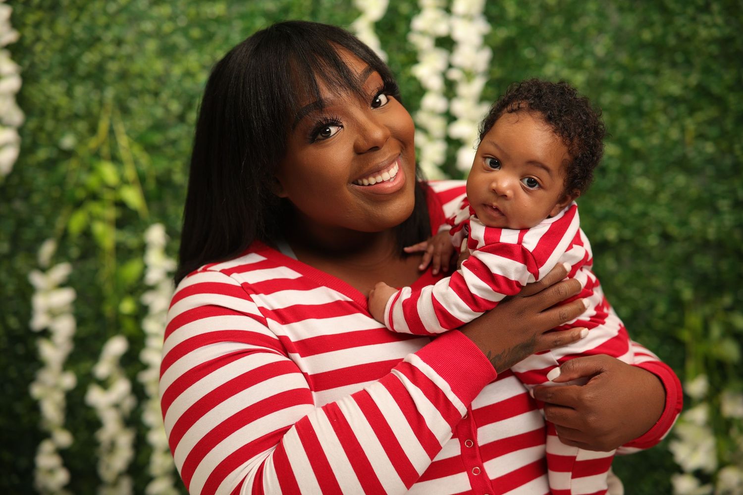 Joyful mother in red striped pajamas holding her newborn baby during Christmas photoshoot.