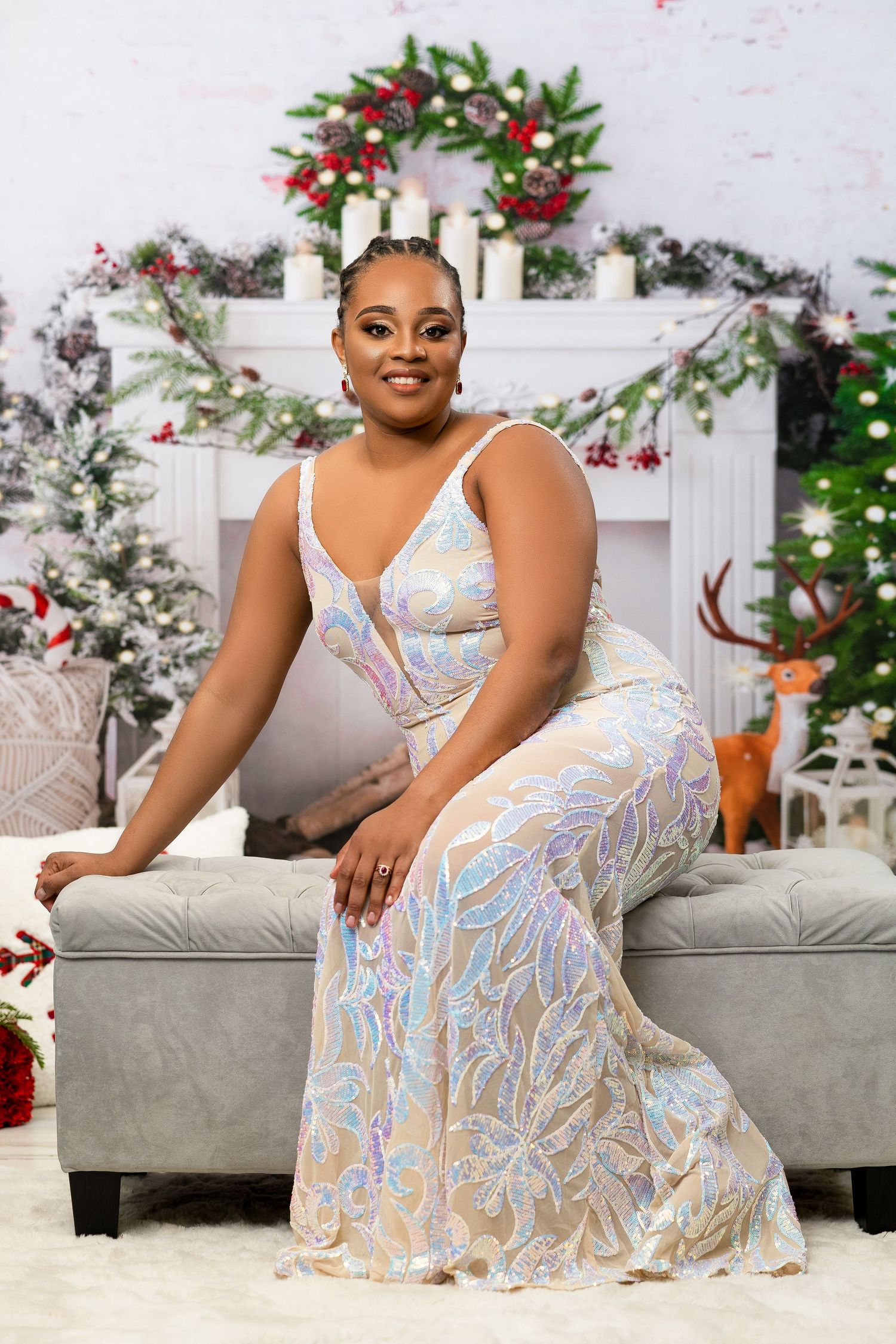 Woman in elegant iridescent gown seated on bench with Christmas tree and fireplace backdrop.
