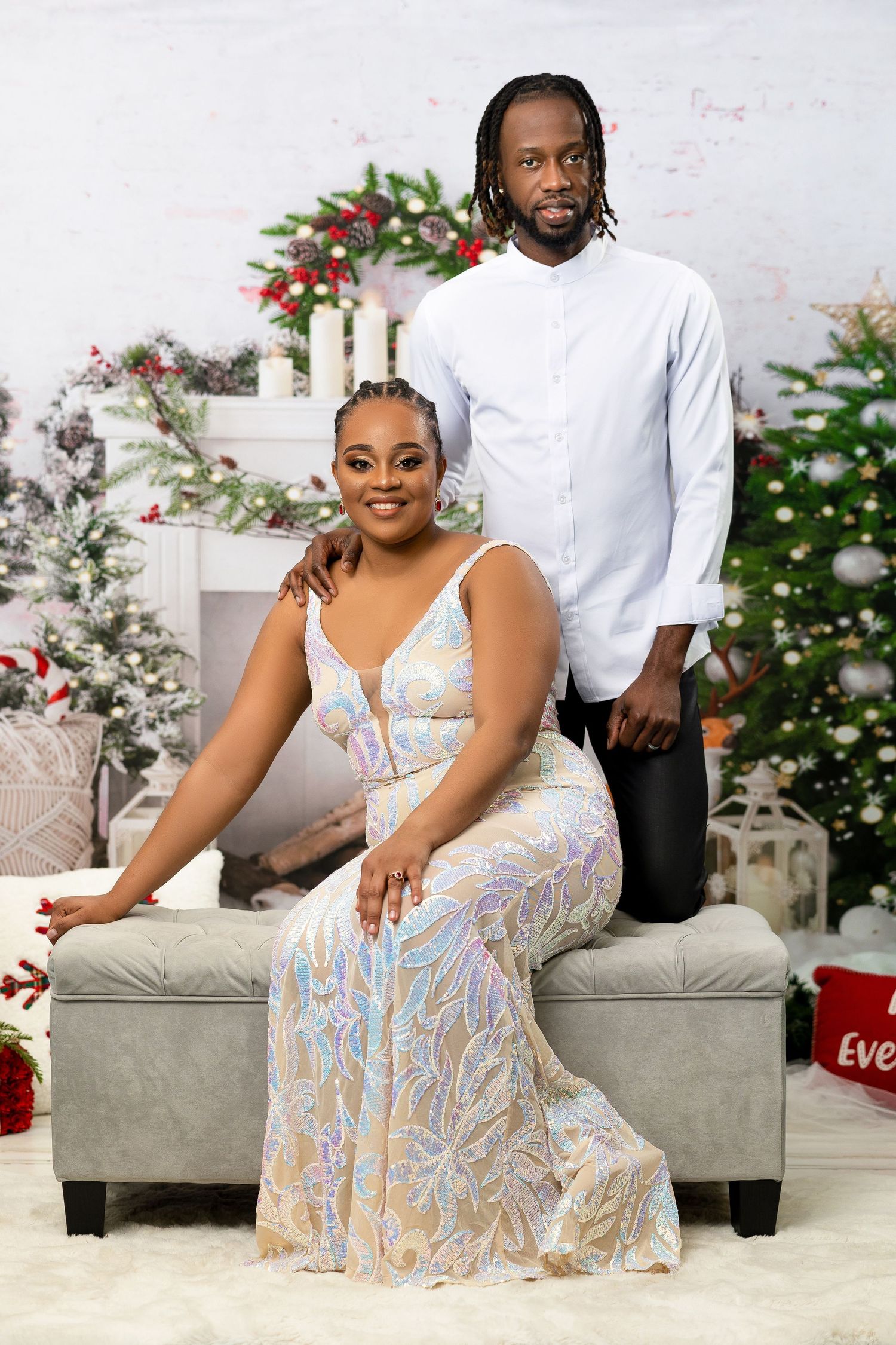 Couple posing elegantly in front of a decorated Christmas tree and fireplace holiday backdrop.