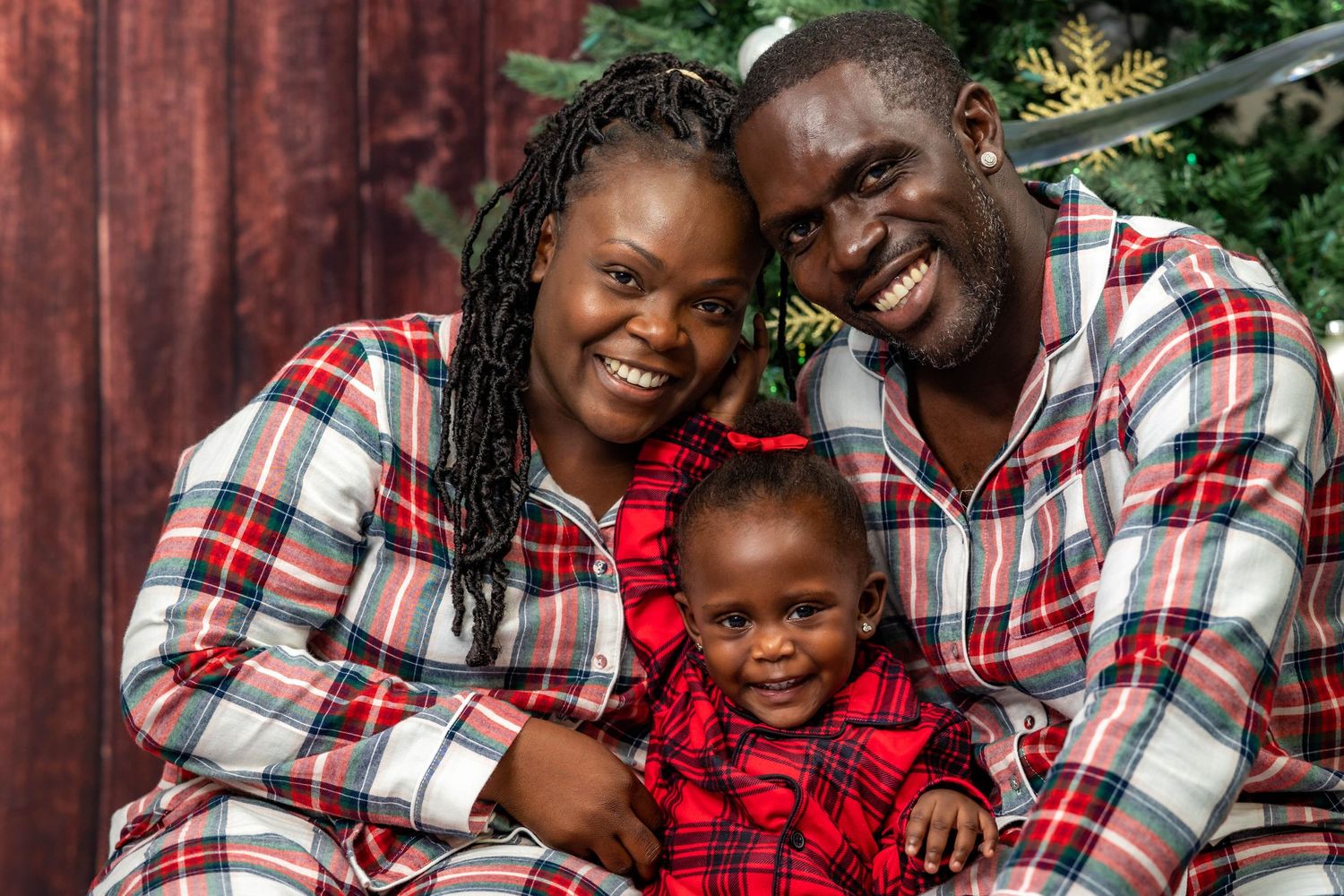 Smiling family in matching plaid Christmas pajamas posing together by holiday decorations.