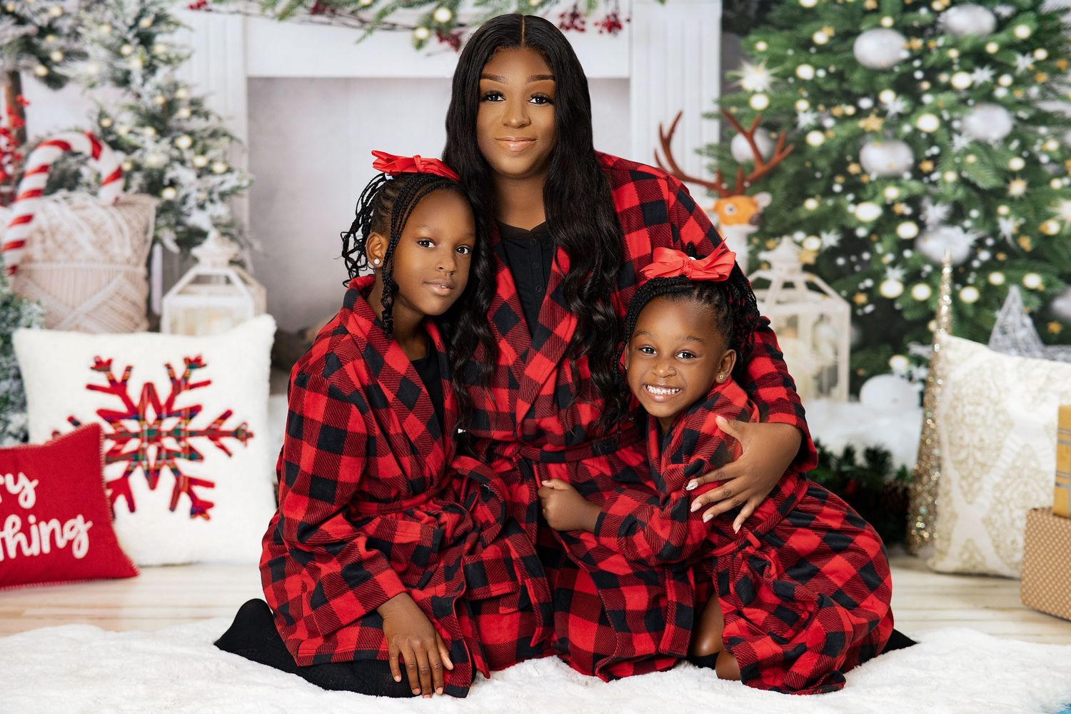 Mother and two children in red plaid robes by Christmas tree.