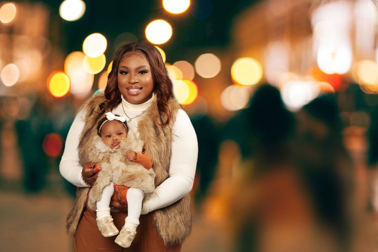 Smiling woman in fur vest holding adorable baby outdoors at night with bokeh lights background.