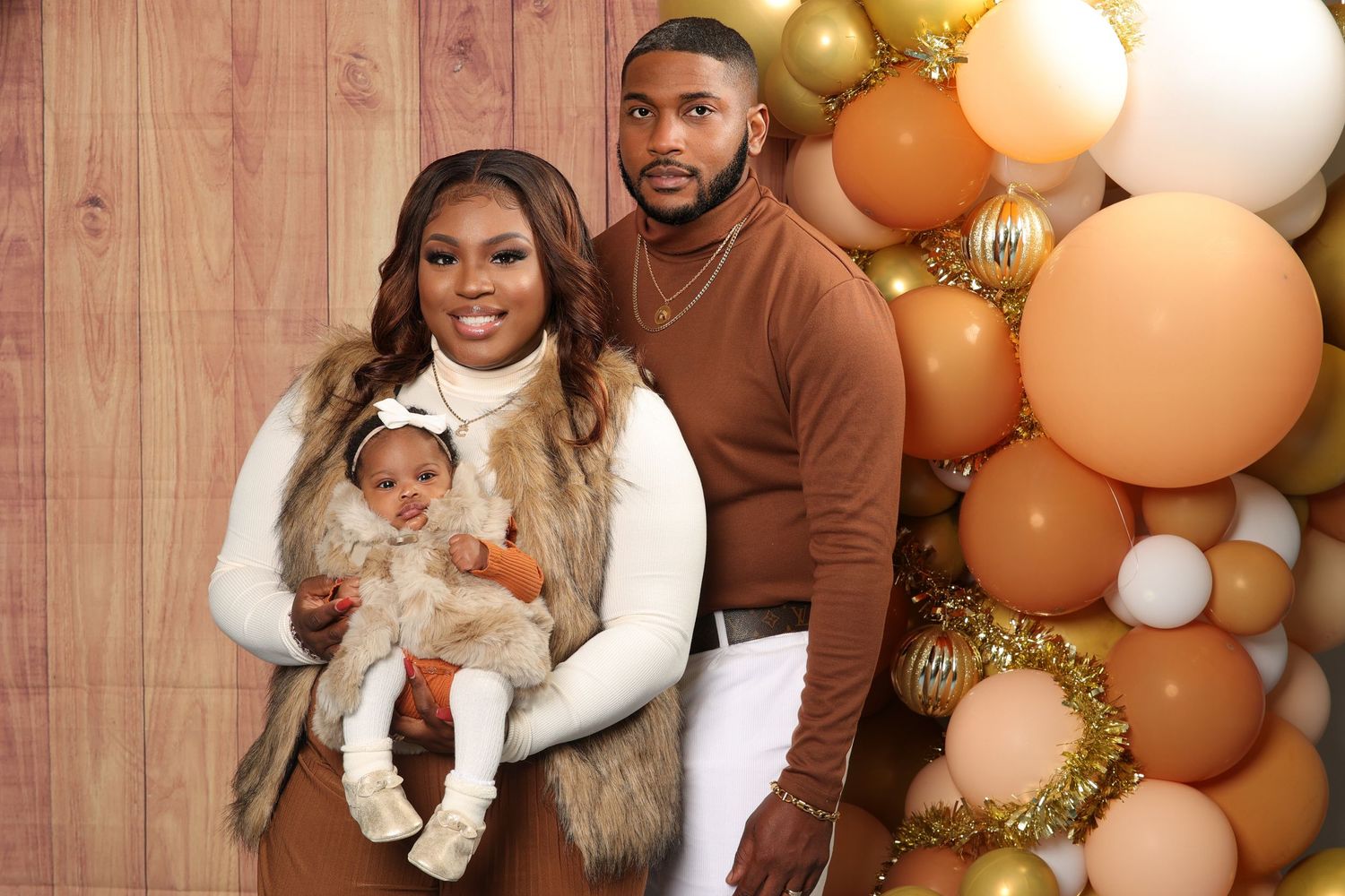 Young couple holding newborn baby in front of balloon garland in neutral fall tones.