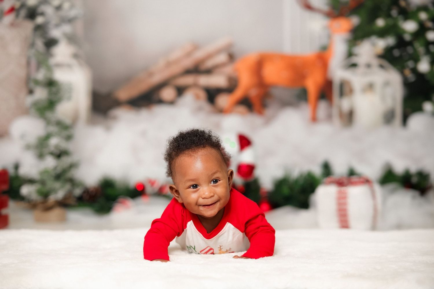 Smiling baby in red Christmas outfit lying on white fur rug.