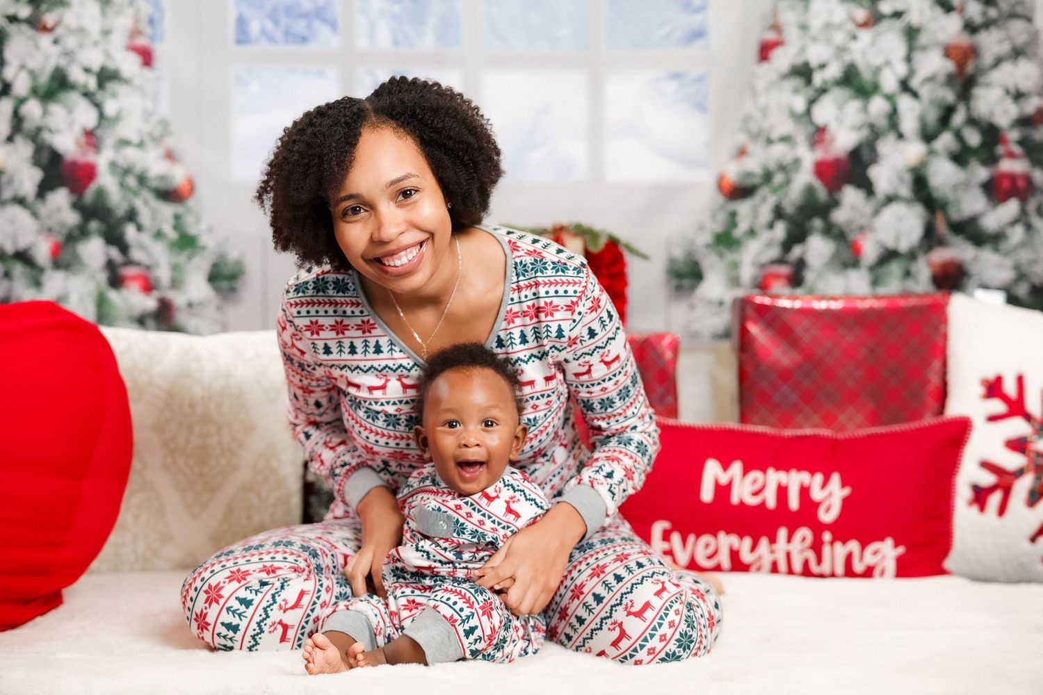 Mother and baby in matching Christmas pajamas by a decorated tree.