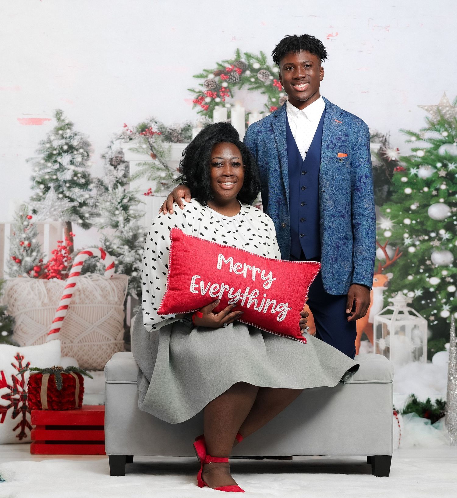 Mother and son posing with Merry Everything pillow in front of Christmas tree backdrop.