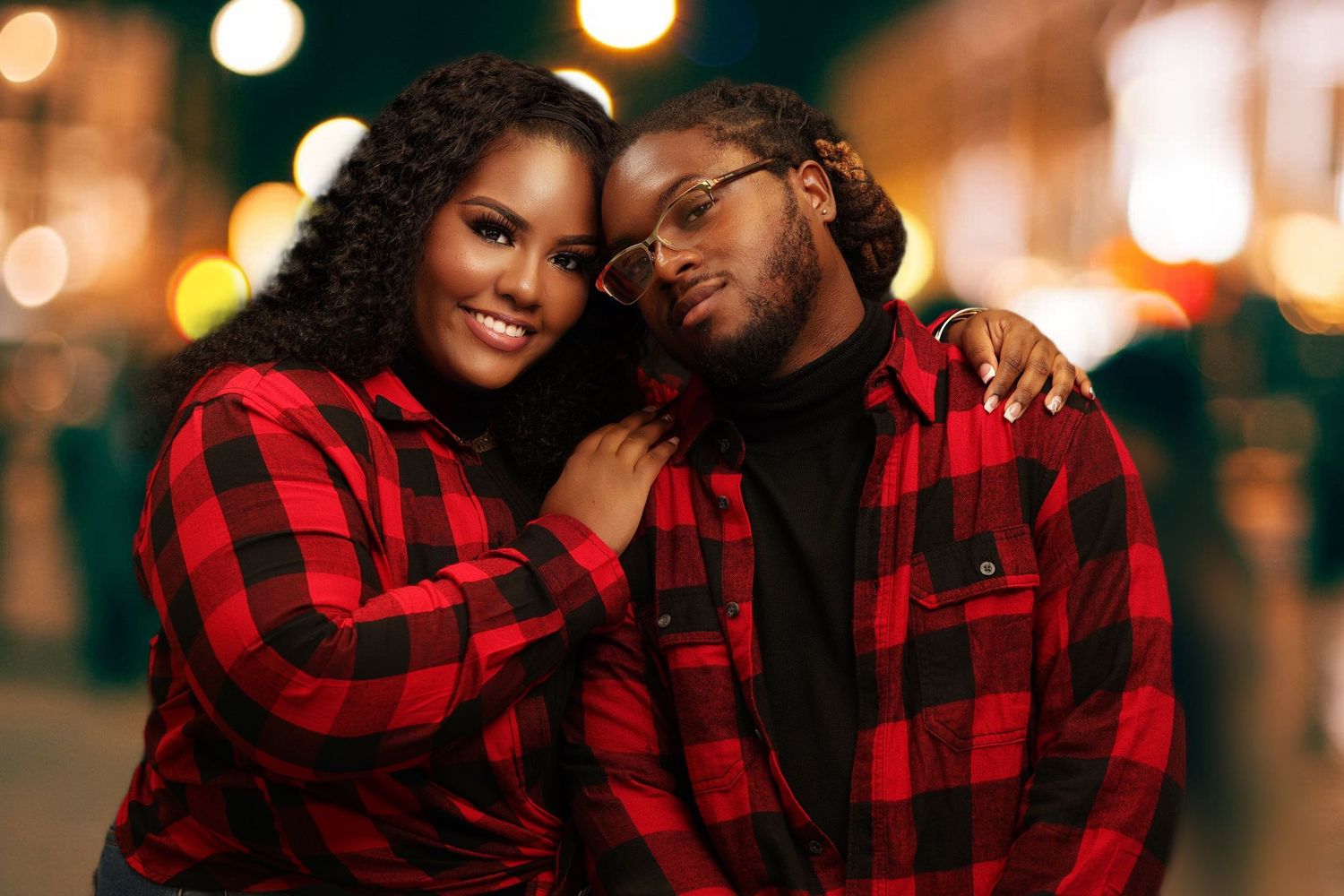 Romantic couple in matching red plaid shirts embracing and smiling at night with bokeh background.
