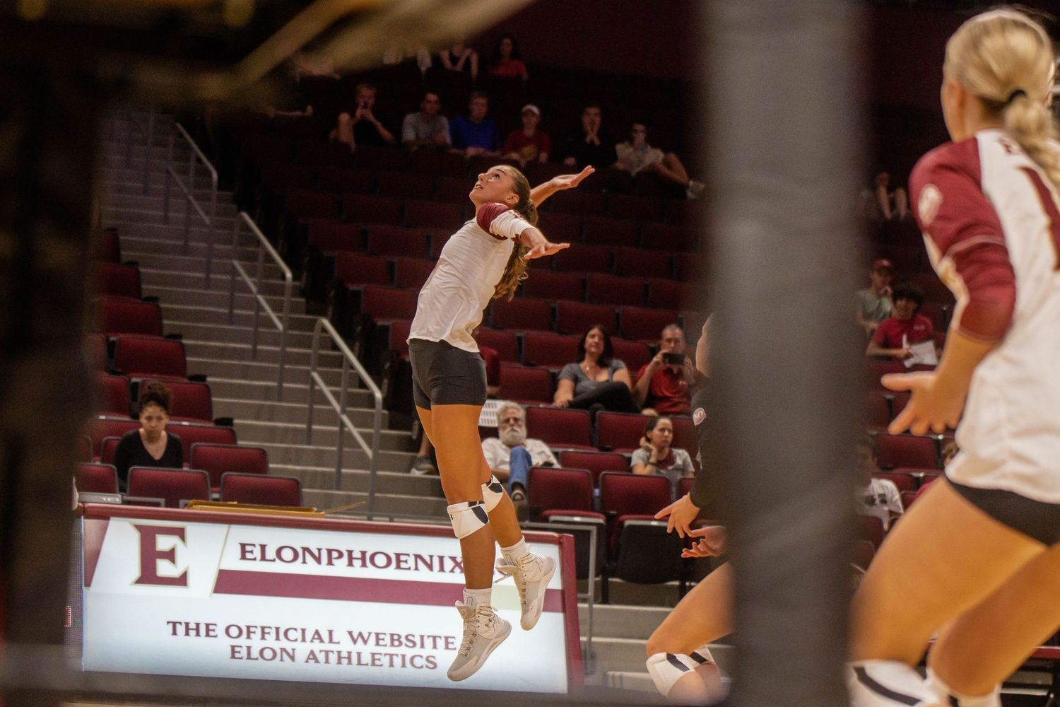 Volleyball player leaps high for a serve in an indoor arena.