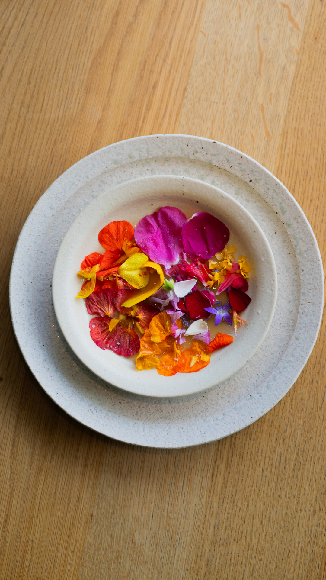 Vibrant edible flowers in pink, orange, and purple arranged in a white ceramic bowl.