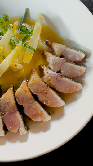 Perfectly seared tuna medallions arranged with white asparagus and herbs in a golden broth.