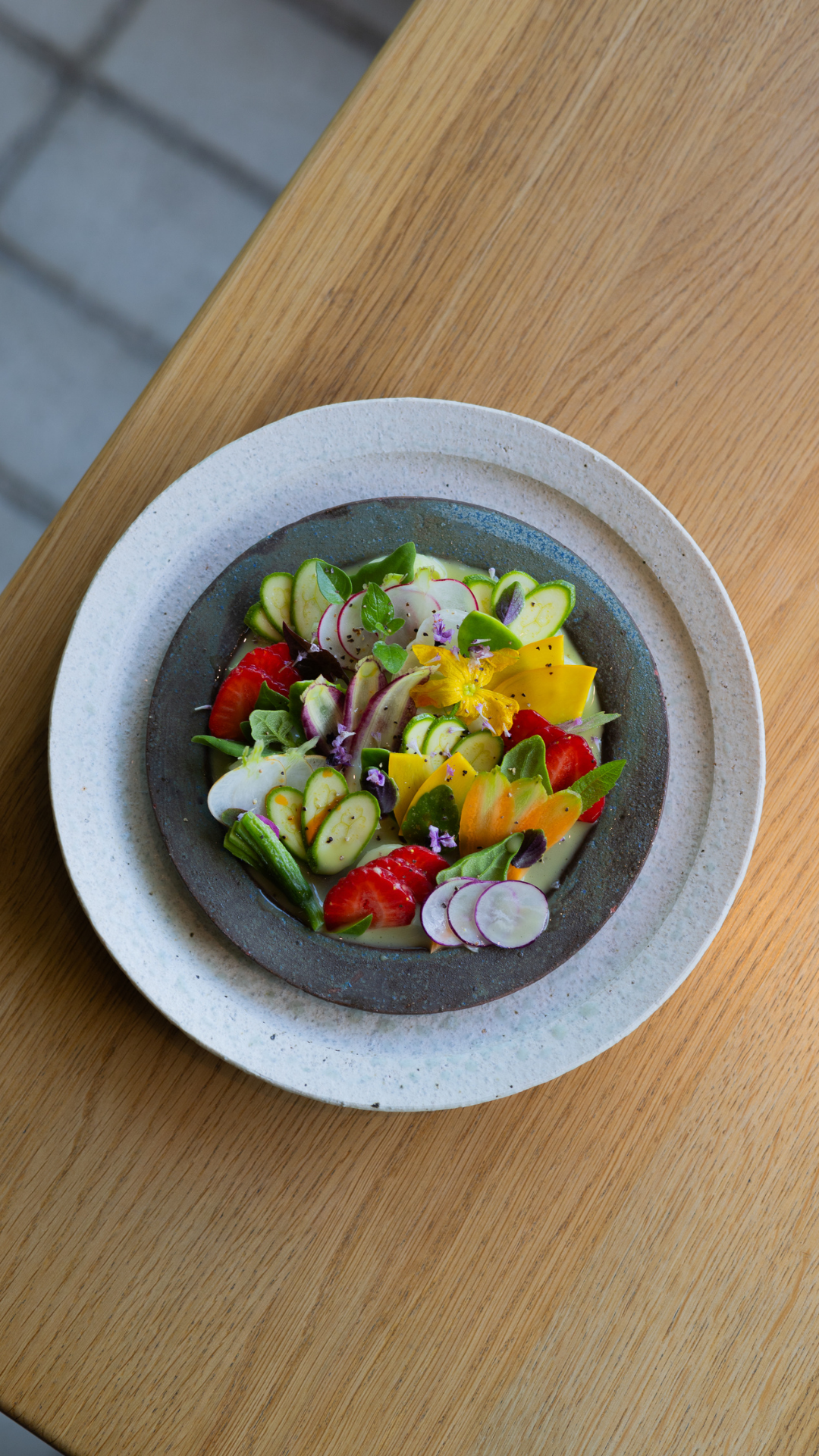 Colorful fresh garden salad with sliced radishes, yellow peppers, and mixed vegetables on a grey plate.