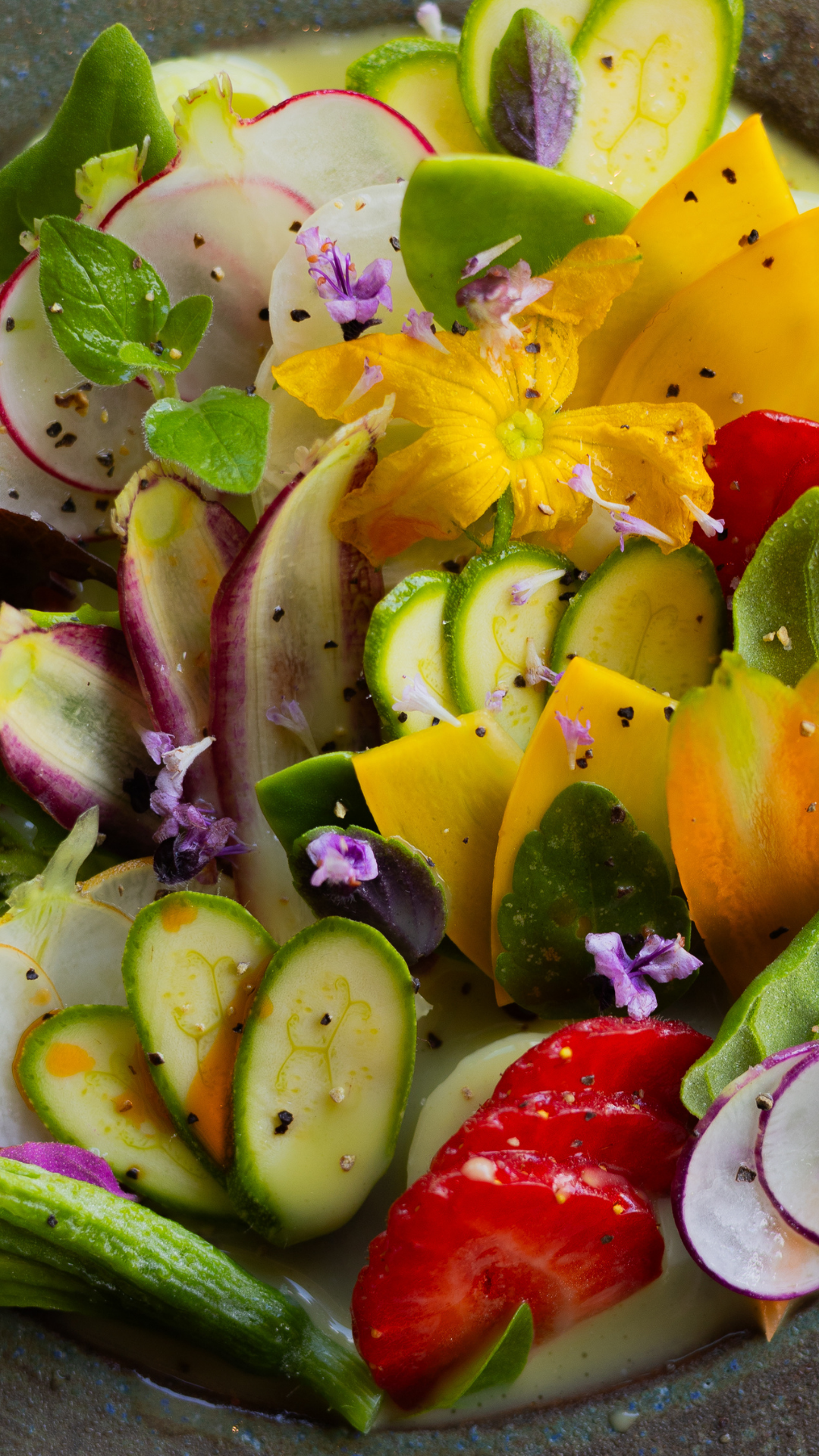 A vibrant salad of sliced vegetables, edible flowers, and radishes with colorful garnishes.