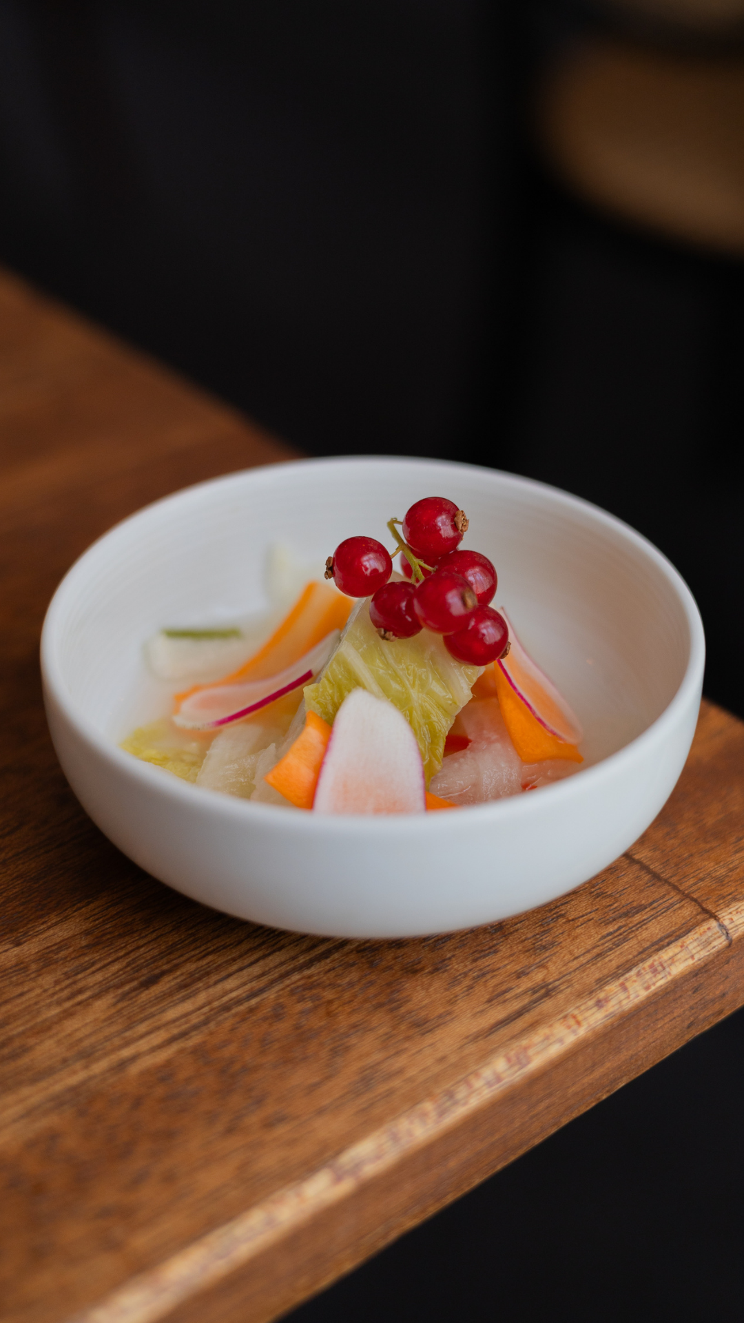 An artistic arrangement of fresh fruits and red currants in a minimalist white bowl.