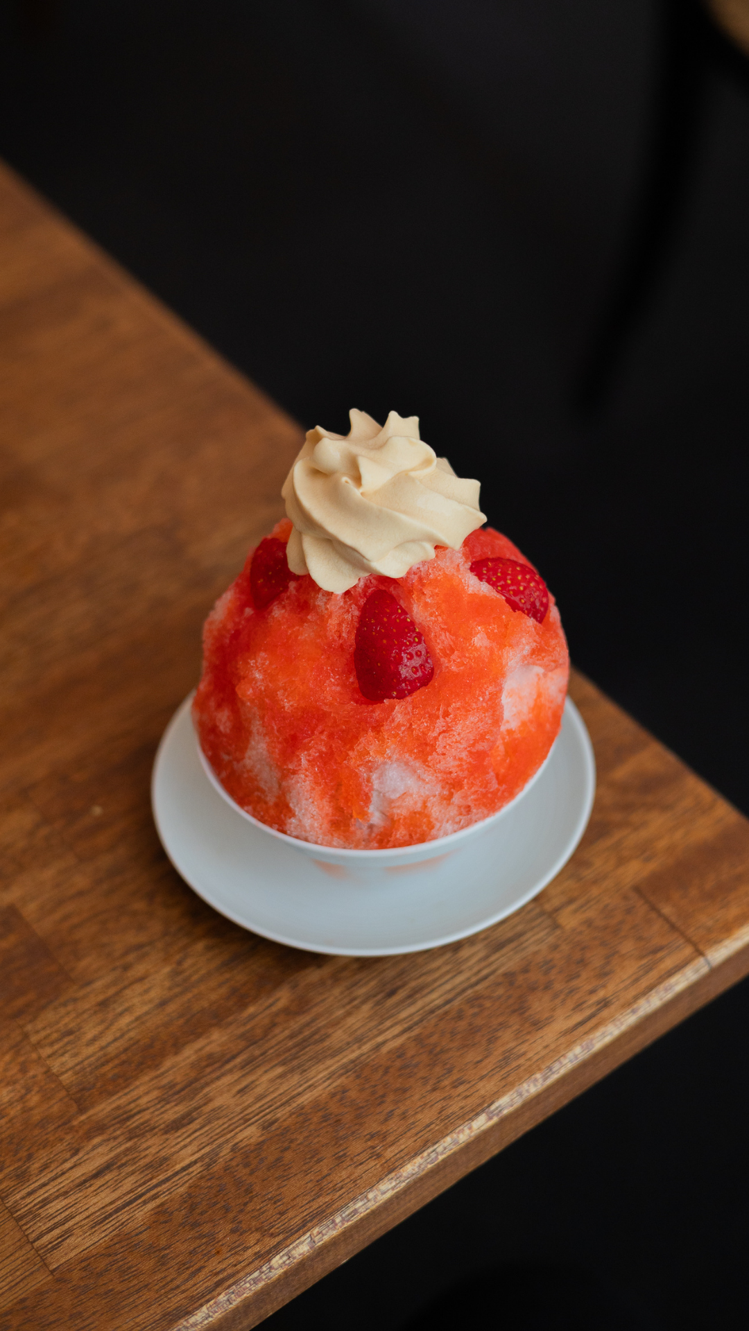 A vibrant red shaved ice dessert garnished with whipped cream and fresh strawberries.
