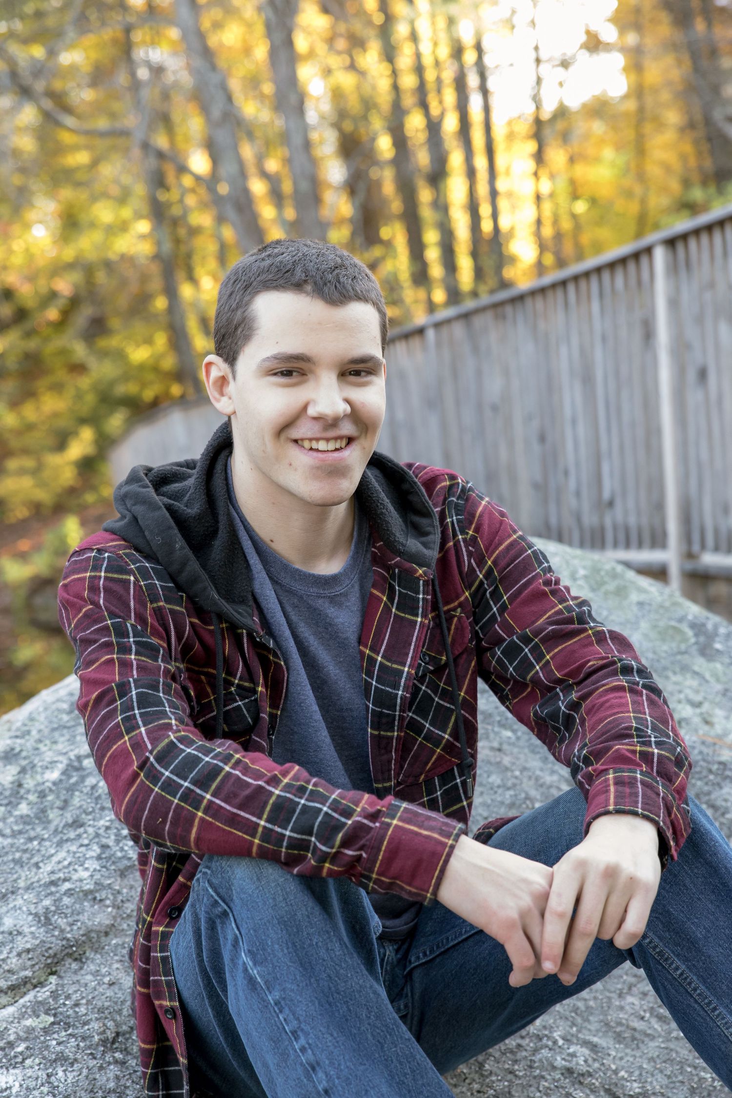 young mans senior portrait  sitting on a foot bridge red plaid shirt jeans  Barnstead NH.