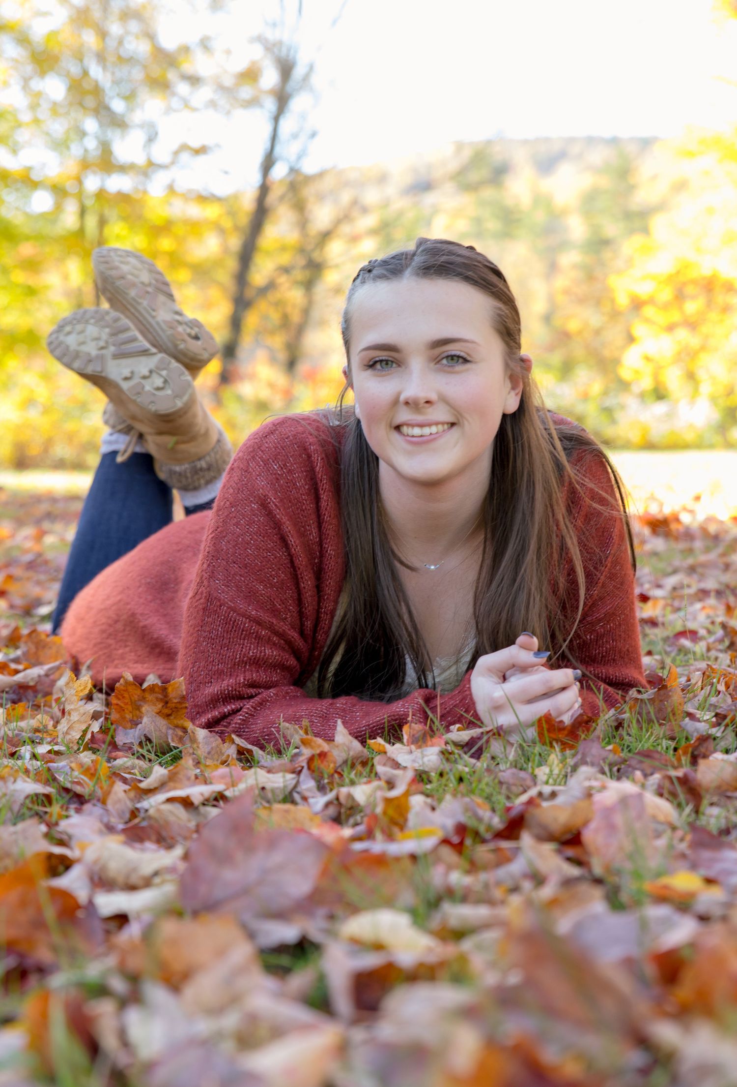 young women's Photography session laying on freshly fallen leaves with yellow trees in back.New Durham NH.