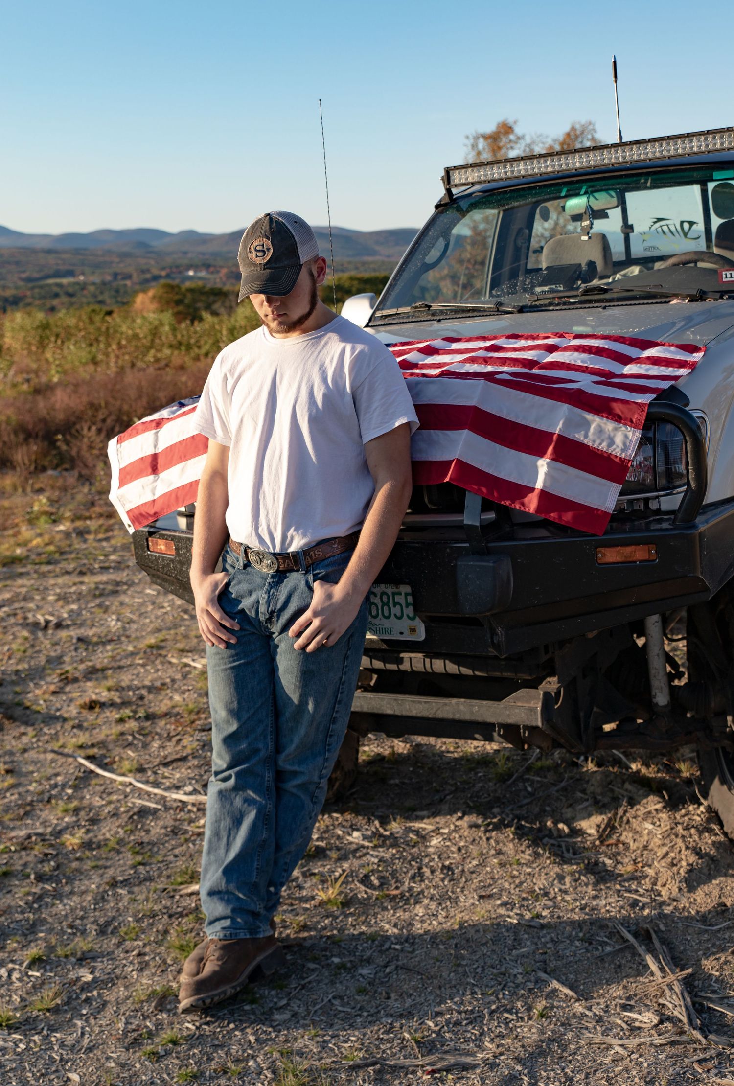 young mans senior portrait with a american flag covered truck whit tee jeans  Barnstead NH.