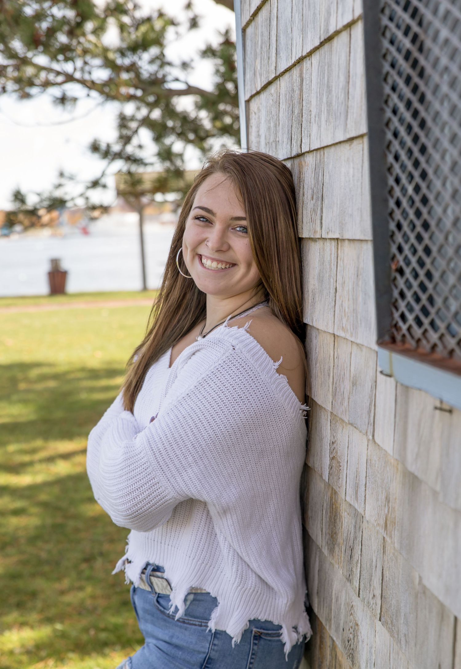 senior girl leaning on the barn wall lake in background white sweater