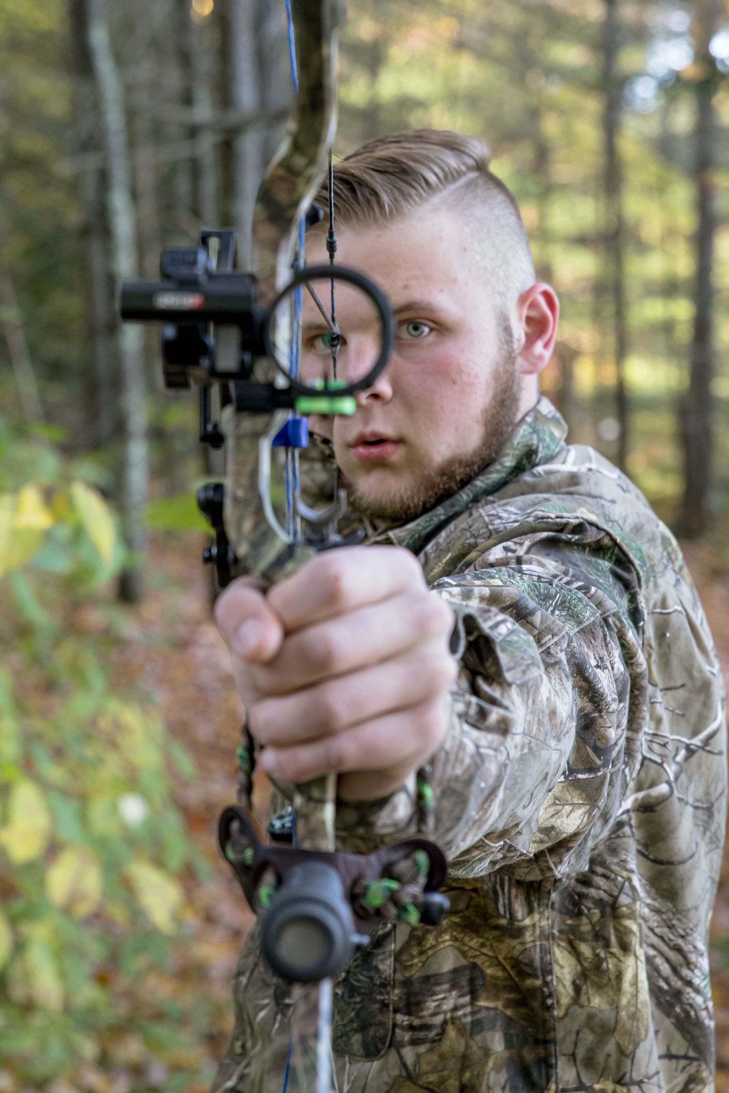 HS senior picture with hunting bow drawn and aimed at the camera  camo shirt short hair. gilford NH