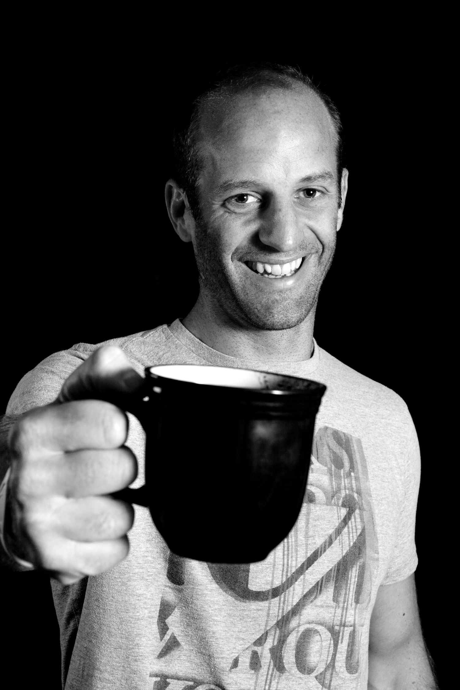 Black and white portrait of person holding large coffee mug with friendly smile during business branding photoshoot.