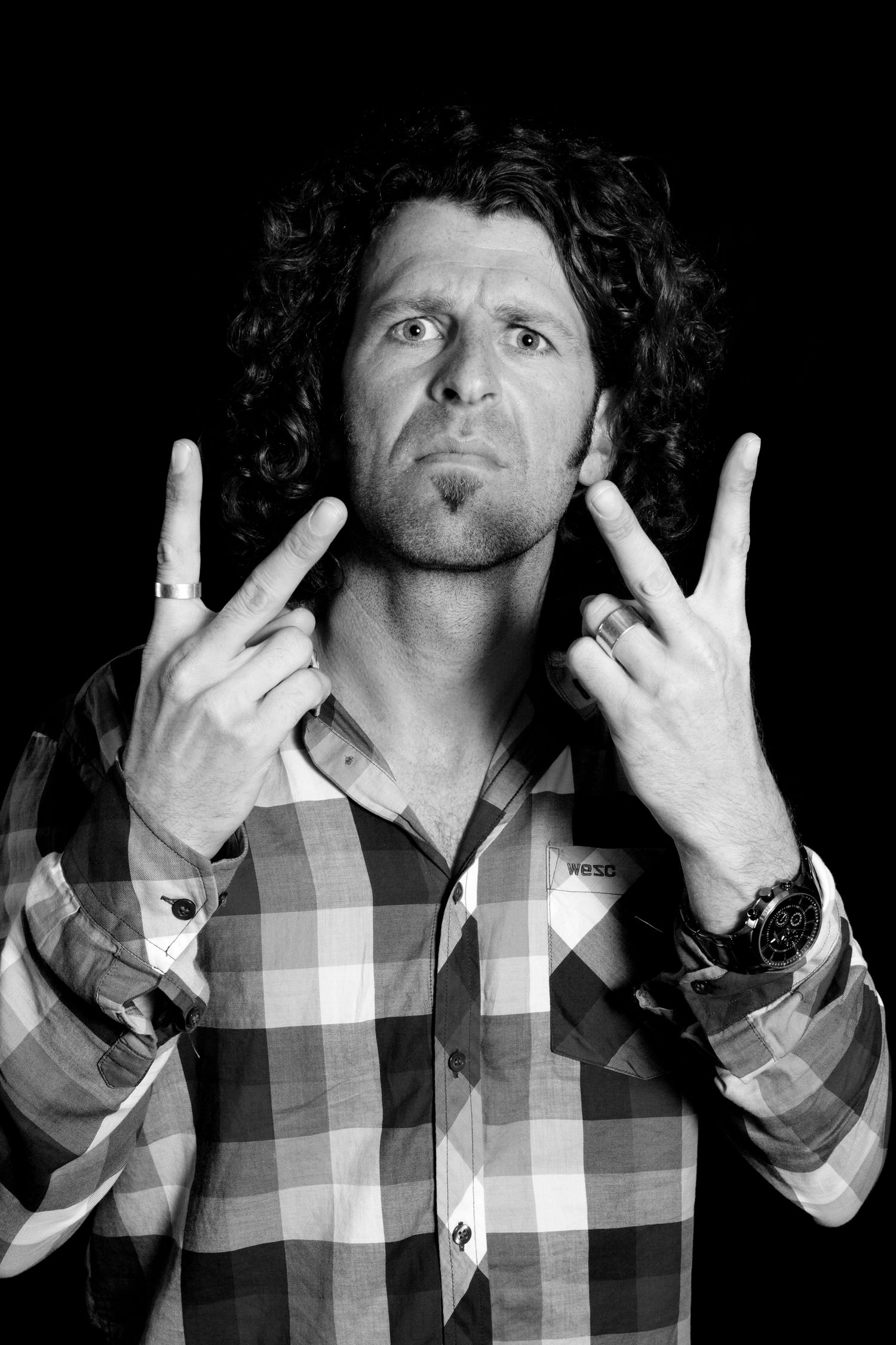 Black and white portrait of person with curly hair making rock gesture against dark background during business branding photoshoot.