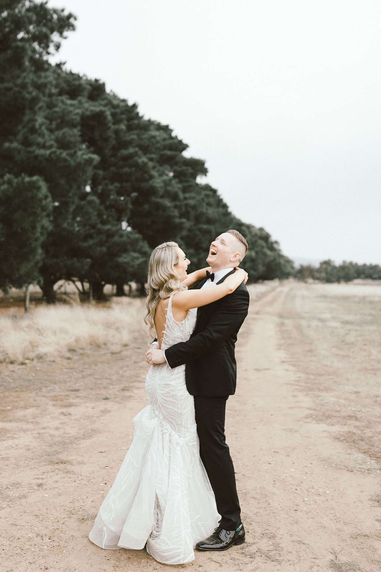 A joyful wedding couple embracing on a countryside dirt road.