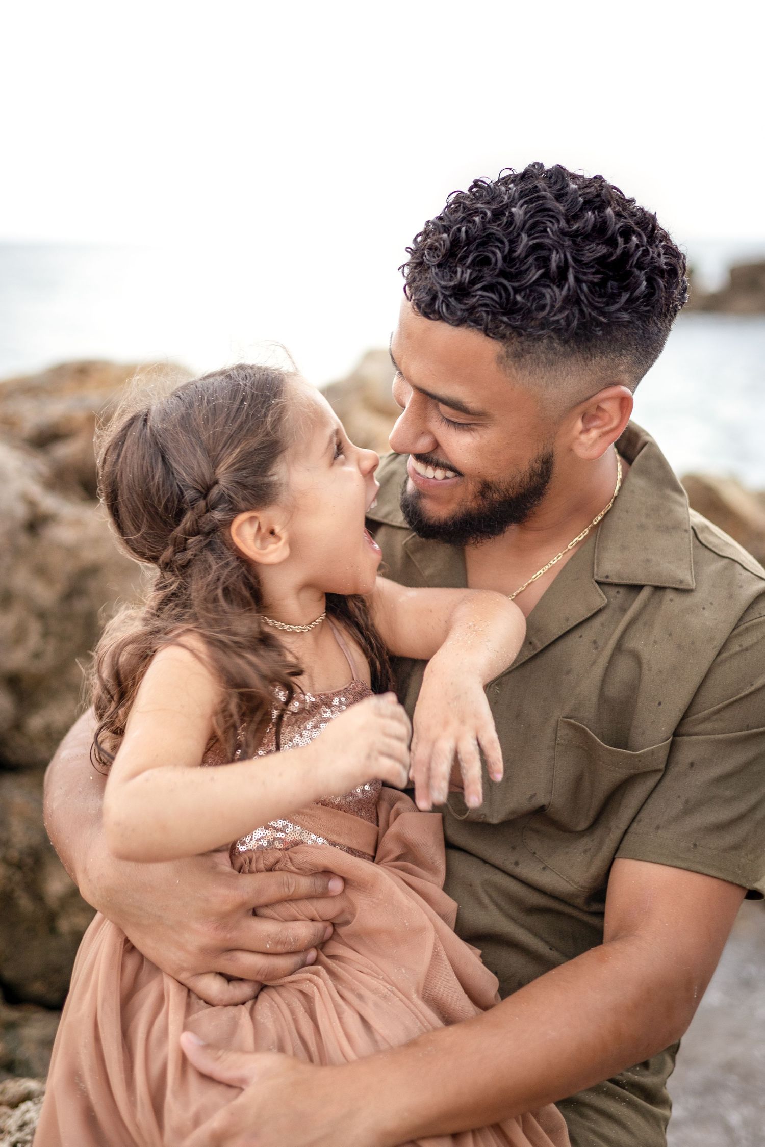 A tender moment of affection between parent and child at a beach setting with rocks in background.