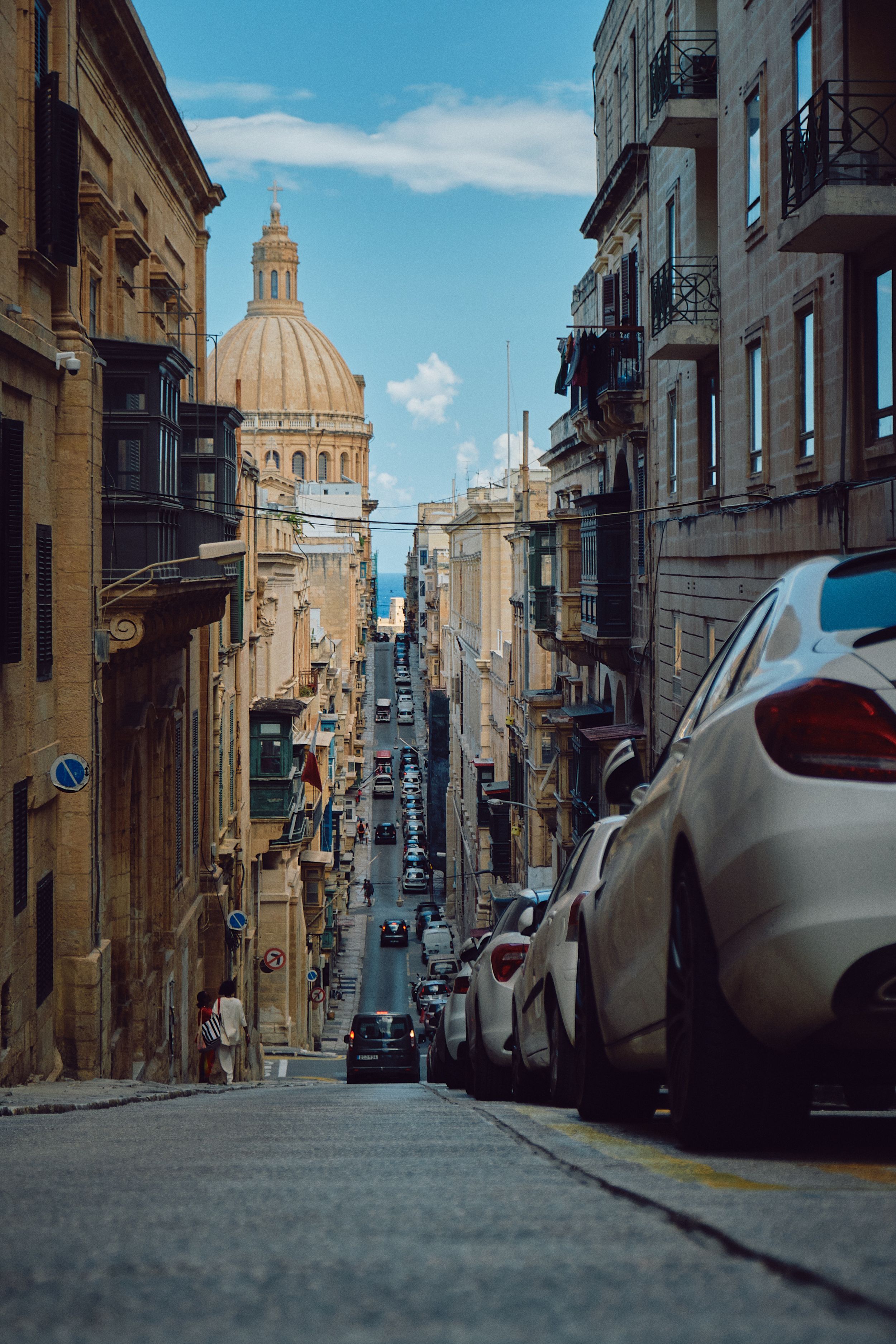 Steep street in Valletta leading to the iconic St. Paul's Cathedral dome against blue sky.