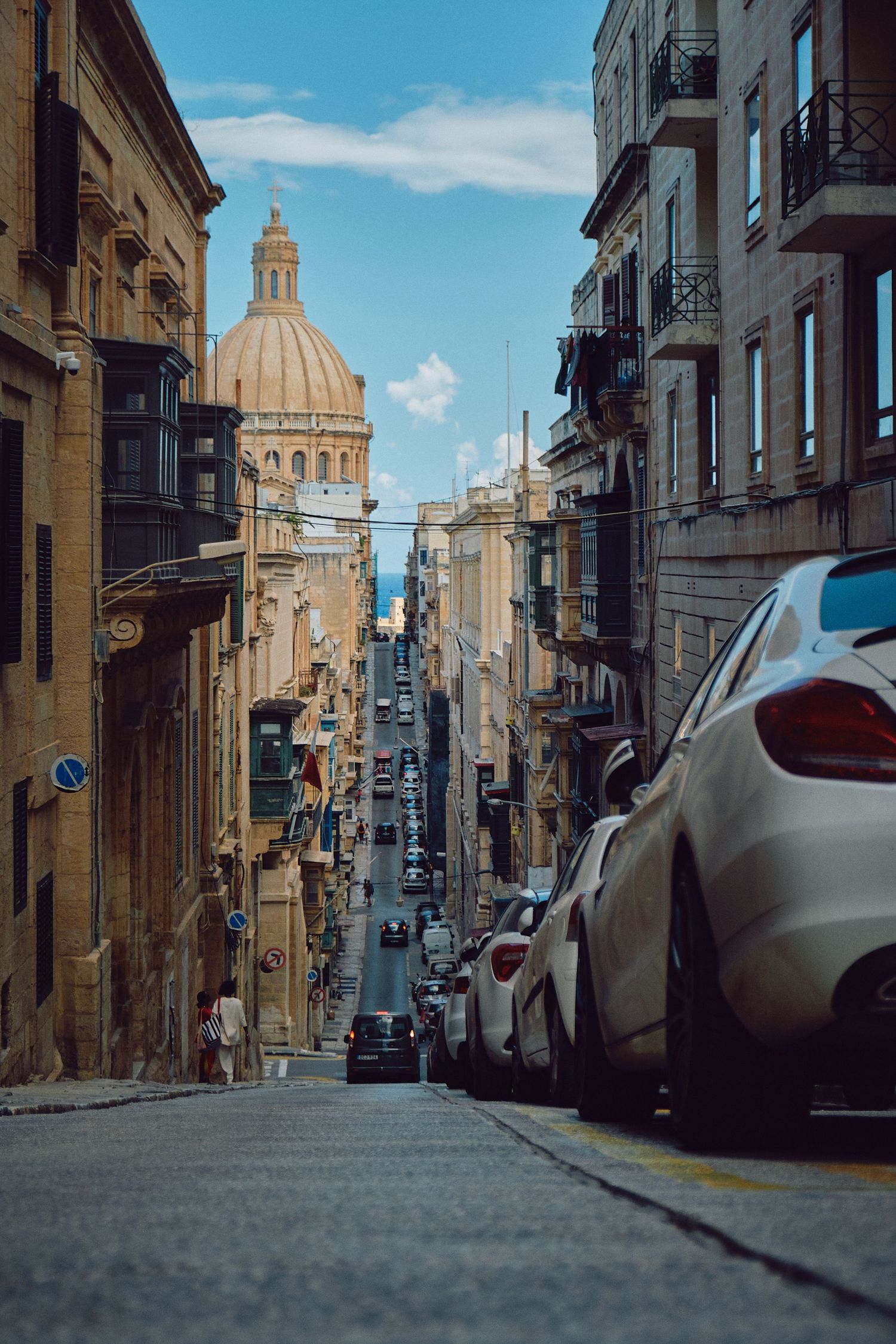Steep street in Valletta leading to the iconic St. Paul's Cathedral dome against blue sky.