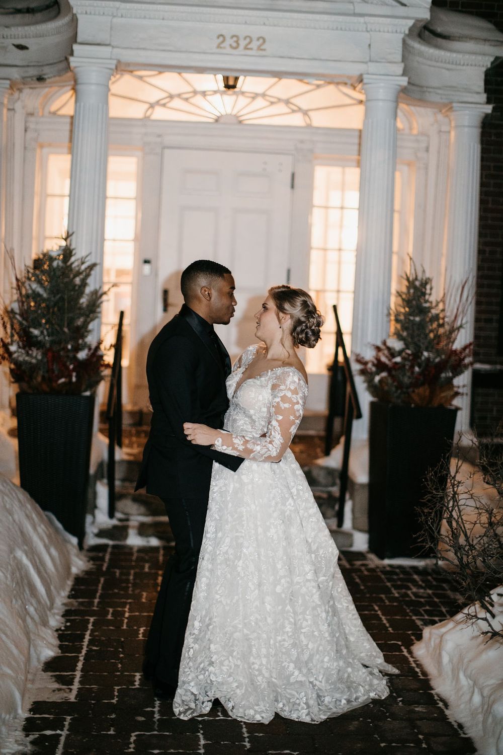 Newlyweds share romantic moment outside historic building number 2322 with winter evening backdrop.