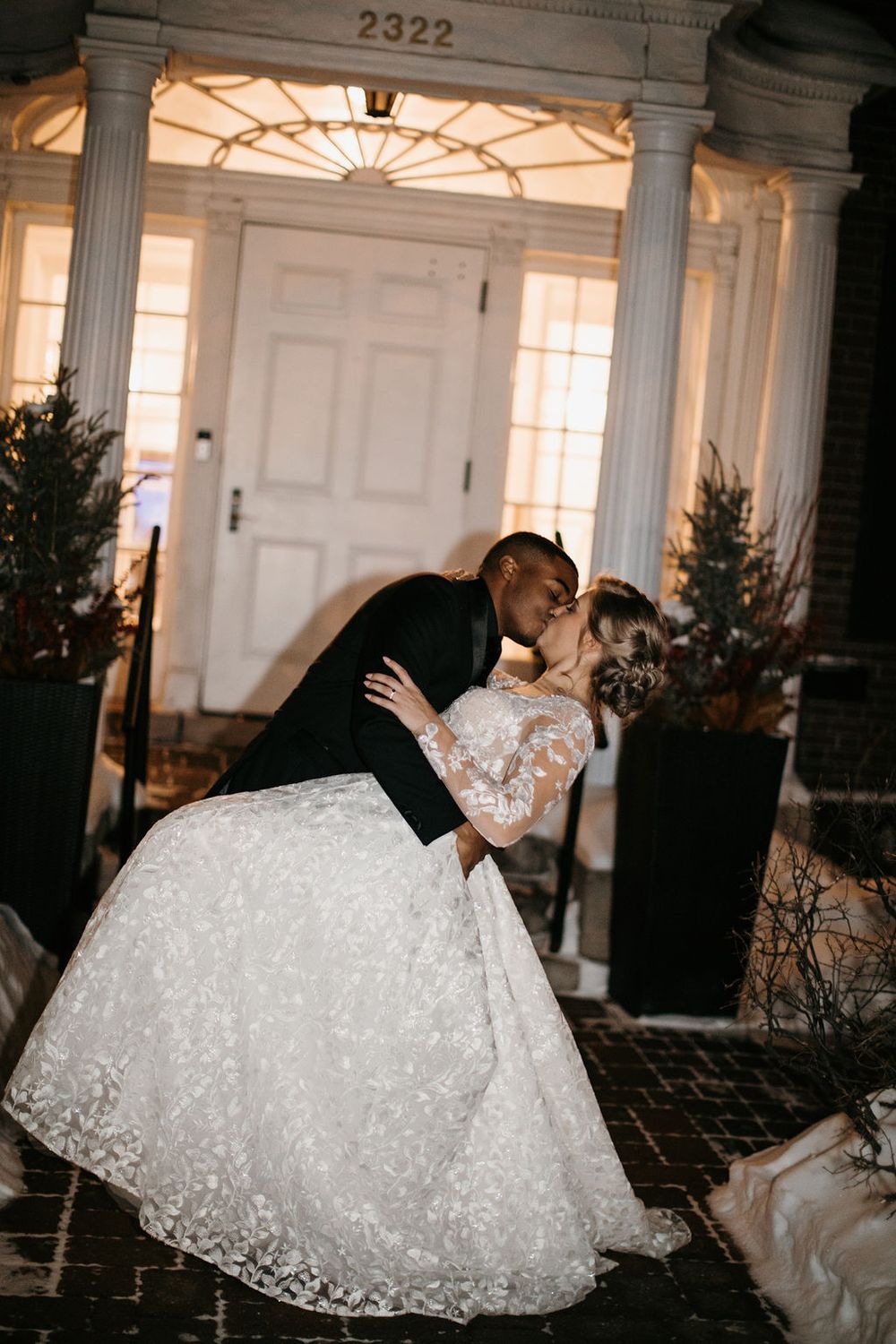 Groom dips bride for a kiss outside illuminated wedding venue entrance at night.