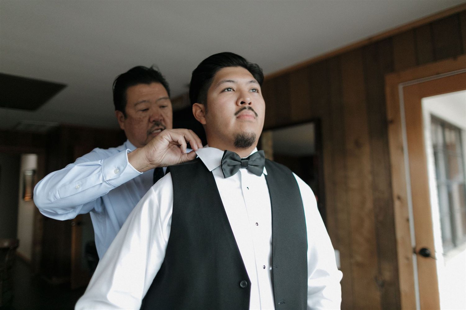 A bowtie being adjusted in a wood-paneled room with natural lighting.
