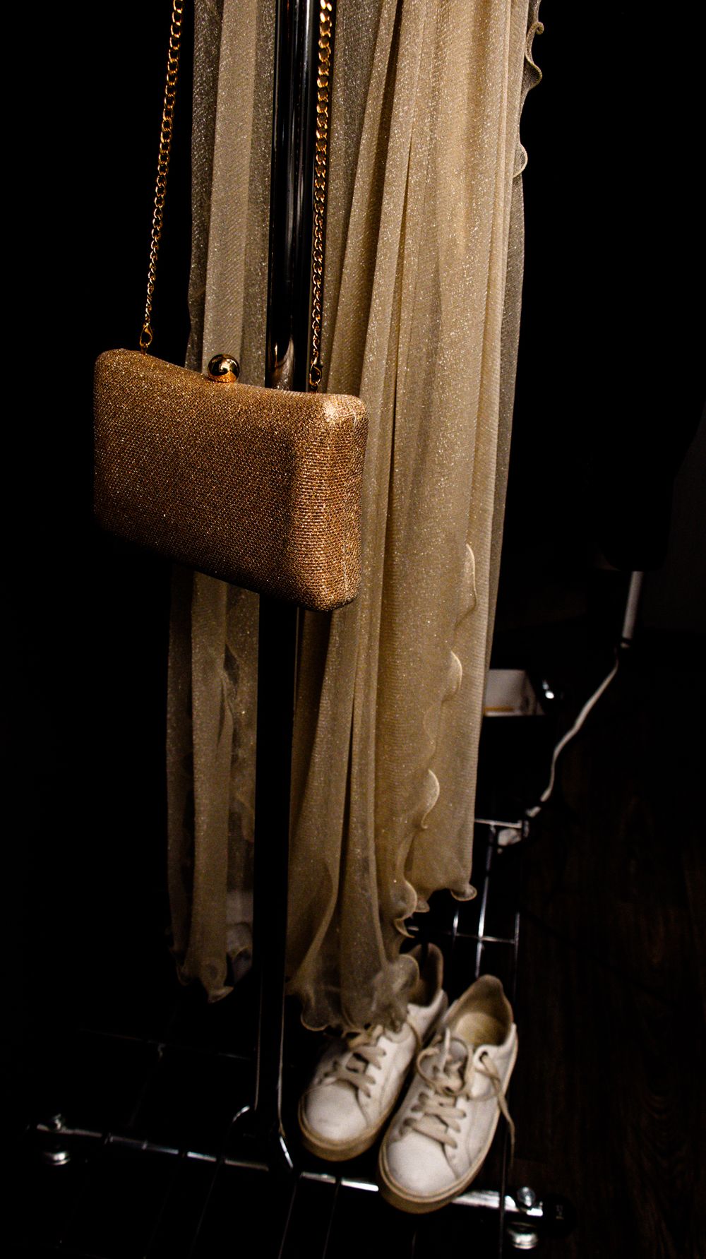 A gold sequined handbag and white sneakers displayed against a dark curtain backdrop.