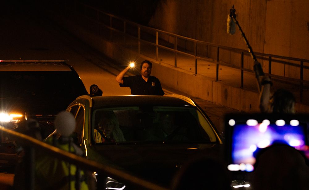 Nighttime scene showing illuminated vehicle with emergency lights visible in background.