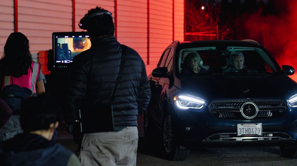 Cars parked in a lot with red lighting casting shadows across the scene.