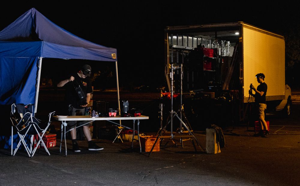 Outdoor event setup at night with blue tents and equipment visible.