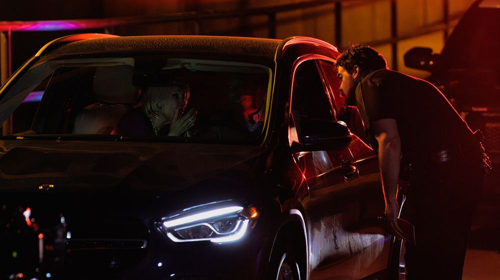 Emergency lights cast red and blue reflections on a dark street during police activity.