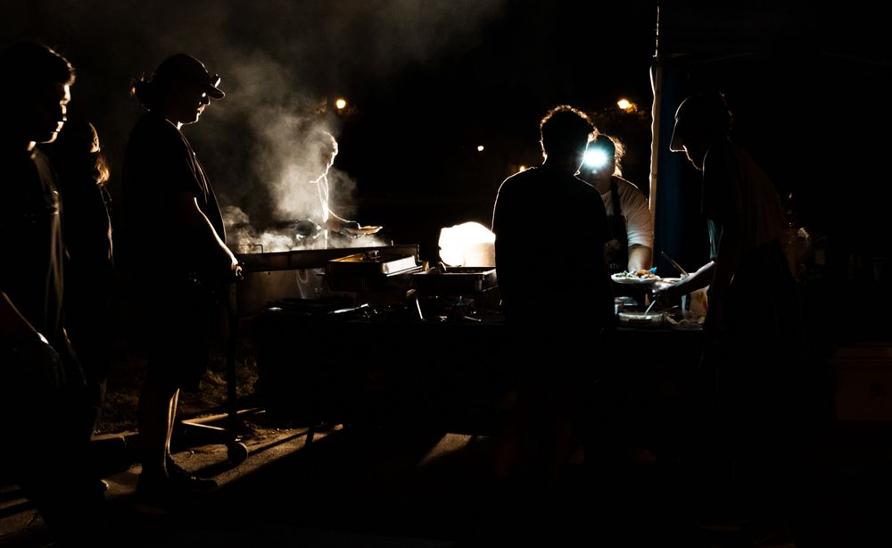 Silhouettes of film crew members working around equipment in dark atmospheric lighting.