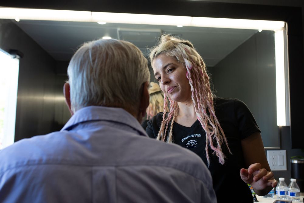 Behind-the-scenes view of makeup application in a brightly lit dressing room.