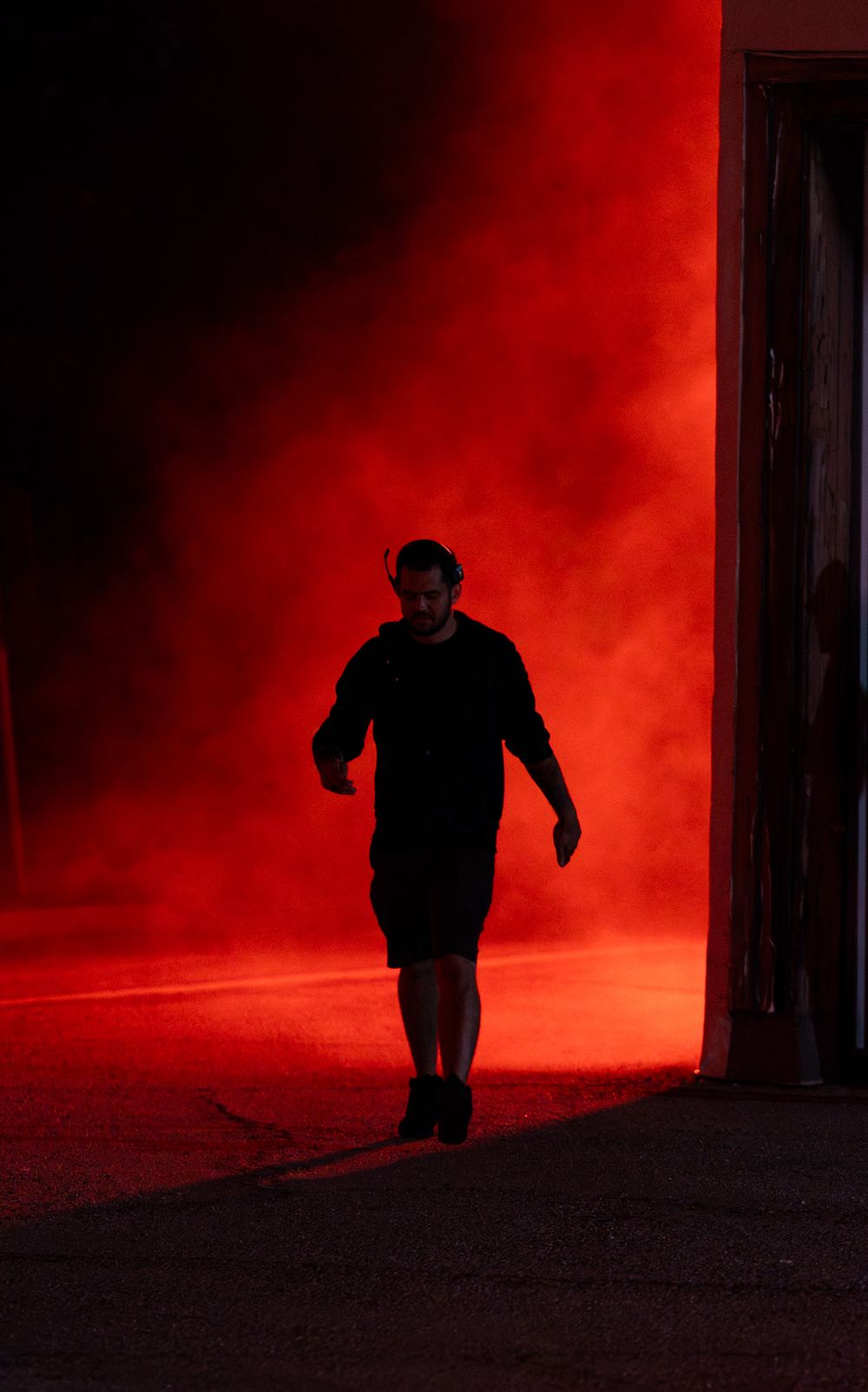 Silhouettes emerge through dramatic red fog in dark urban setting at night.