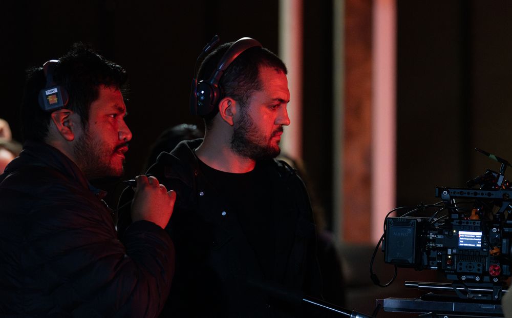 Film crew operating cameras in dark setting with red accent lighting.