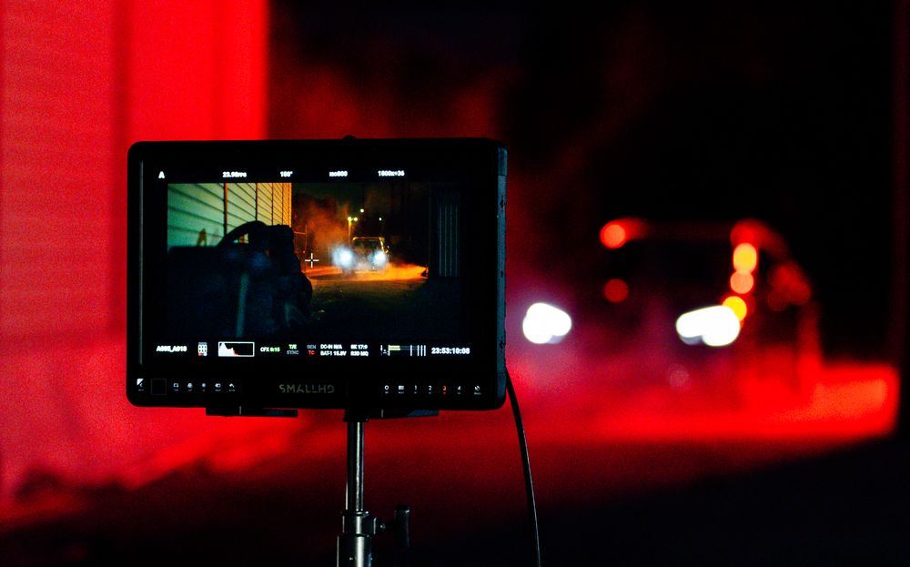 Red emergency lights illuminate dark scene with video monitor visible.