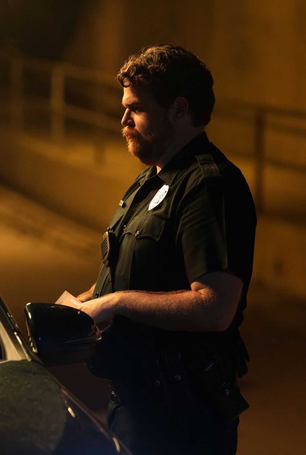 Police officer writes notes while standing in amber street lighting.
