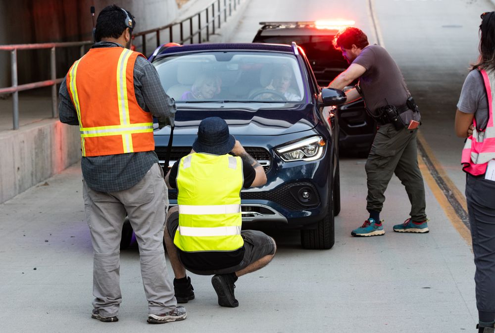 Safety personnel in high-visibility vests directing traffic around a black Mercedes vehicle.