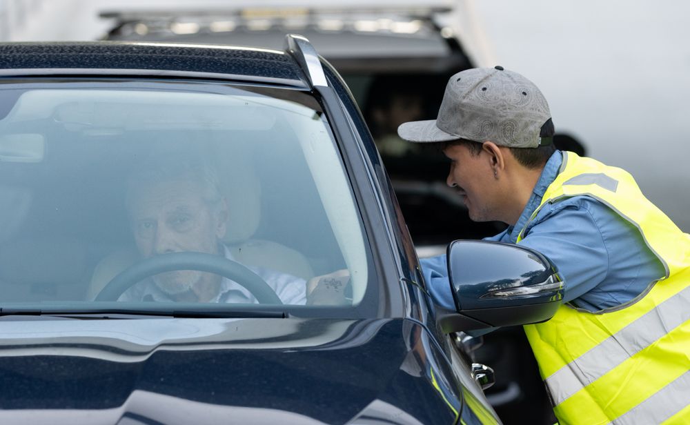 Safety worker in yellow reflective vest leans to speak with vehicle occupant through car window.