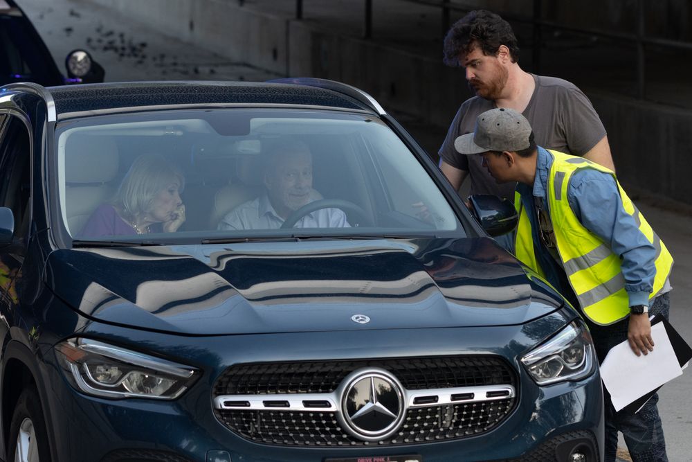 Black Mercedes vehicle with safety personnel in reflective vests nearby.
